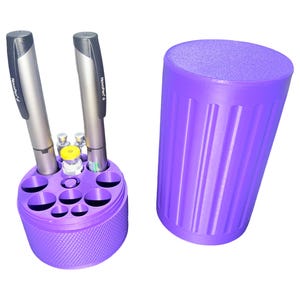 May include: A purple medical supply organizer with a matching cylindrical case. The organizer holds two silver insulin pens and several small vials. The organizer has multiple circular openings of varying sizes. The case has vertical grooves.