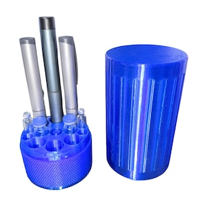 May include: A blue 3D-printed organizer with a cylindrical design, holding pens and small vials. A separate blue cylindrical lid is next to the organizer. The organizer has a textured base and is designed to hold various items.
