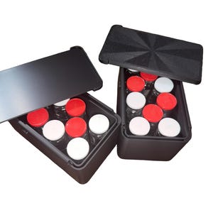 May include: Two rectangular black storage cases with lids, each containing multiple small clear glass jars. The jars have either solid red or solid white screw-on caps. The lids of the cases are black, with one featuring a textured starburst pattern.