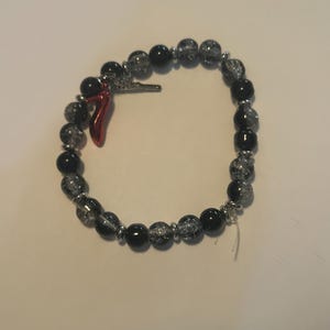 May include: A beaded bracelet featuring black and clear crackle beads, interspersed with silver-toned spacers. A small red horn charm and a silver-toned charm are attached. The bracelet is designed to be worn around the wrist.
