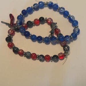 May include: Three beaded bracelets. One bracelet features blue beads, another has red, black, and gray beads, and the third has a mix of blue, red, black, and gray beads. All bracelets have silver-colored metal accents.