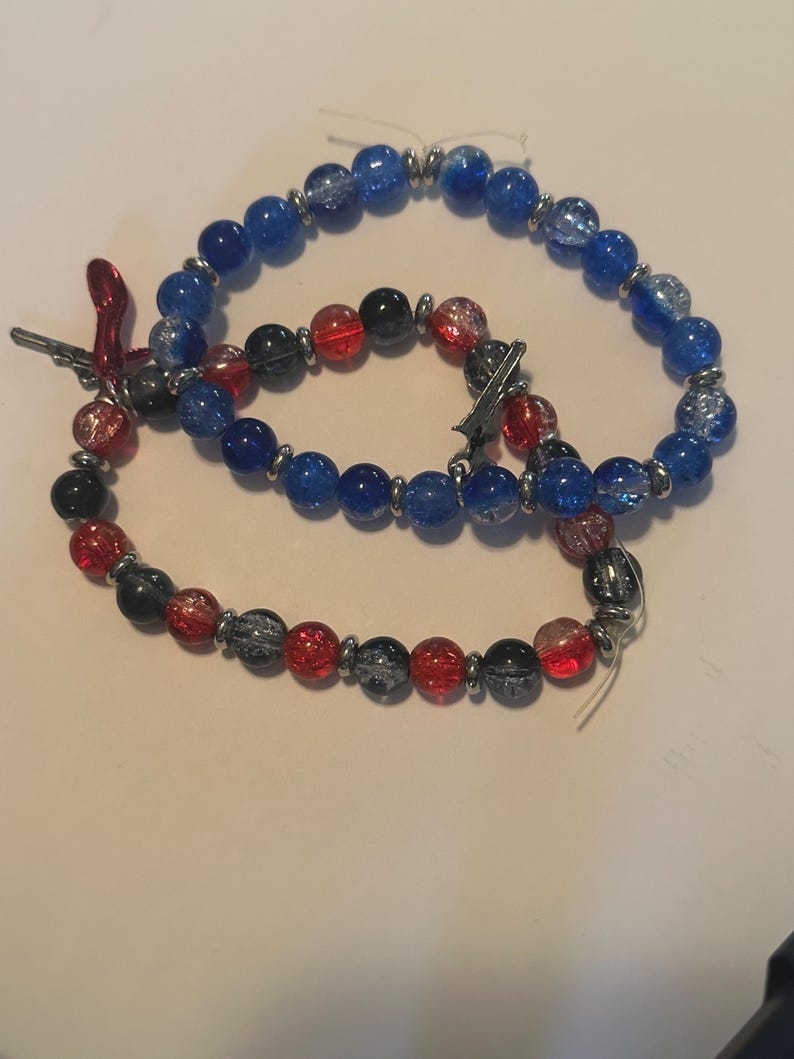 May include: Three beaded bracelets. One bracelet features blue beads, another has red, black, and gray beads, and the third has a mix of blue, red, black, and gray beads. All bracelets have silver-colored metal accents.