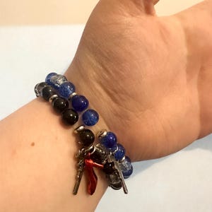 May include: Two beaded bracelets with charms. One bracelet features black and blue beads, the other has black and blue beads with silver accents. Charms include silver keys and a red high-heeled shoe.