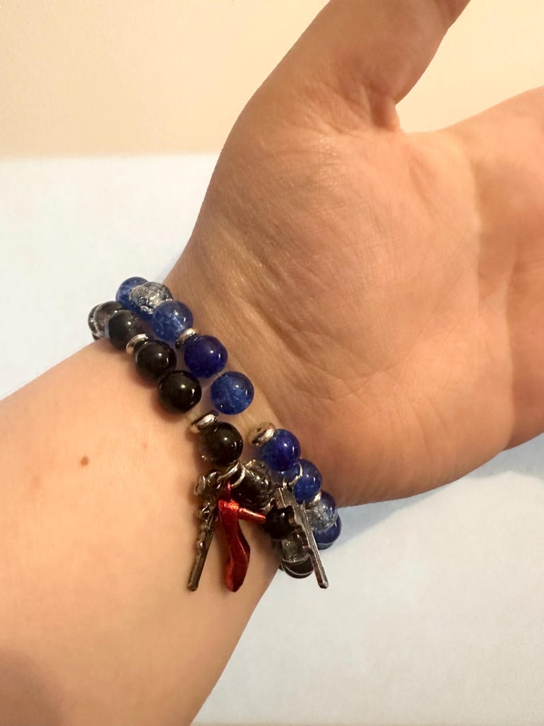 May include: Two beaded bracelets with charms. One bracelet features black and blue beads, the other has black and blue beads with silver accents. Charms include silver keys and a red high-heeled shoe.