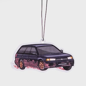 May include: A car-shaped air freshener featuring a dark blue station wagon with gold-colored wheels. The car has a stylized design with red and pink accents, and is suspended by a black string.