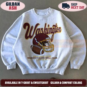 May include: An ash grey crewneck sweatshirt featuring a distressed graphic of a burgundy football helmet and a brown football. The text reads Washington, Property of the Washington Football Club, and Est. 1932 in burgundy and gold lettering.