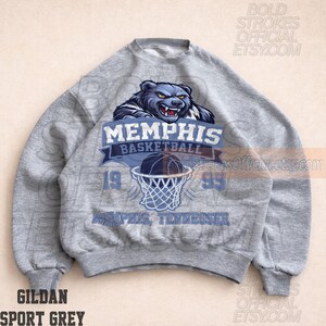 May include: A gray Gildan Sport Grey sweatshirt featuring a Memphis Basketball design. The design includes a blue bear graphic above the text "MEMPHIS BASKETBALL" and a basketball going into a net. The year "1995" is also displayed.
