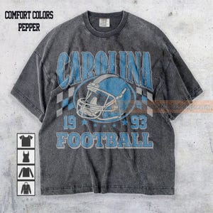 May include: A gray Comfort Colors t-shirt with a distressed Carolina Football design. The design features the word "CAROLINA" in blue, a football helmet, the numbers "19" and "93", and the word "FOOTBALL".