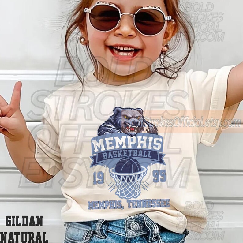 May include: A cream-colored t-shirt featuring a Memphis Basketball graphic. The design includes a bear, basketball, and the text "MEMPHIS BASKETBALL 1995 MEMPHIS, TENNESSEE". The shirt is made of Gildan Natural material.