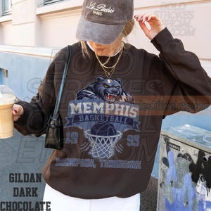 May include: Dark chocolate brown sweatshirt featuring a Memphis Basketball design with a bear graphic, basketball, and net. The text includes "MEMPHIS BASKETBALL" and "1995". The sweatshirt is a Gildan brand.