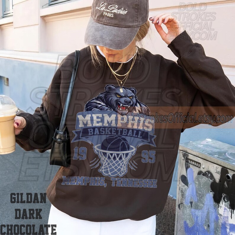 May include: Dark chocolate brown sweatshirt featuring a Memphis Basketball design with a bear graphic, basketball, and net. The text includes "MEMPHIS BASKETBALL" and "1995". The sweatshirt is a Gildan brand.