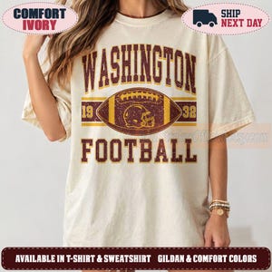 May include: An ivory short-sleeve t-shirt featuring a distressed graphic with the text WASHINGTON FOOTBALL in dark red. A central football illustration contains a helmet icon and the numbers 19 and 32 in a vintage-inspired athletic style.