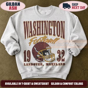 May include: A light grey crewneck sweatshirt featuring a maroon and gold graphic. The text reads WASHINGTON Football 1932 LANDOVER, MARYLAND. A maroon football helmet with a gold face mask is centred below the word Washington.