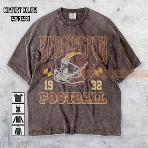 May include: Espresso-colored t-shirt with a vintage-style graphic. The design features the word "WASHINGTON" above a football helmet, the numbers "19" and "32", and the word "FOOTBALL". The shirt has a classic crew neck and short sleeves.