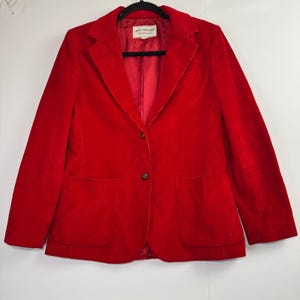 May include: A bright red corduroy blazer featuring a notched lapel, two front buttons, and two large patch pockets. The interior is lined with matching red fabric and includes a white label with the text Jones New York Sportswear.
