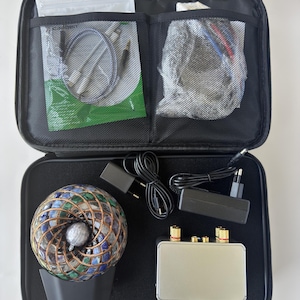 May include: A black zipped carrying case containing a spherical mosaic lamp with blue and green glass tiles, a rectangular silver audio amplifier, two black power adapters with cords, and a clear plastic bag with various audio cables.
