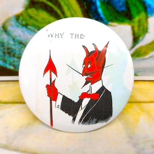 May include: White button badge featuring a cartoon devil in a black suit, holding a red spear. The text "WHY THE" is above the devil. A vintage-style design.