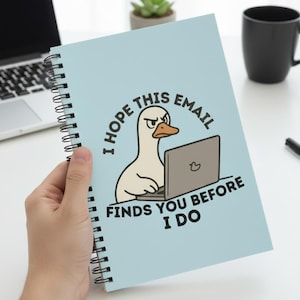 Può includere: Un quaderno a spirale azzurro con la scritta "I HOPE THIS EMAIL FINDS YOU BEFORE I DO" e un'anatra dei cartoni animati che usa un laptop. Il quaderno è tenuto in mano.