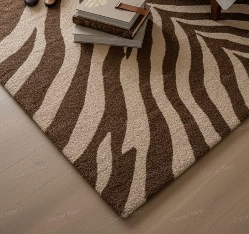 May include: A rectangular rug featuring a zebra stripe design in brown and cream. The rug has a textured surface and is placed on a light-coloured wooden floor. Books are stacked on the rug.