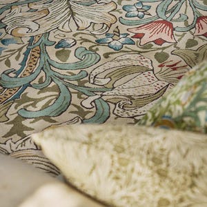 May include: A textile featuring a dense botanical pattern with large cream-colored lilies, swirling sage green foliage, and accents of light blue and muted red flowers. The intricate design covers the surface with overlapping floral motifs.