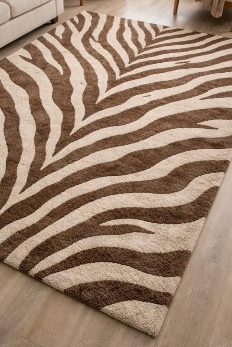 May include: A rectangular rug with a zebra stripe design in brown and beige. The rug has a soft, textured appearance, suitable for a living room or bedroom. The design features wide, irregular stripes.