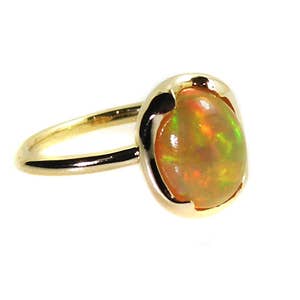 May include: A gold ring with a large oval opal gemstone. The opal has a rainbow of colors, including green, orange, and red.