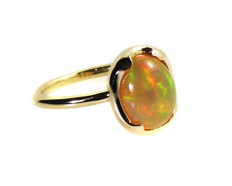 May include: A gold ring with a large oval opal gemstone. The opal has a rainbow of colors, including green, orange, and red.