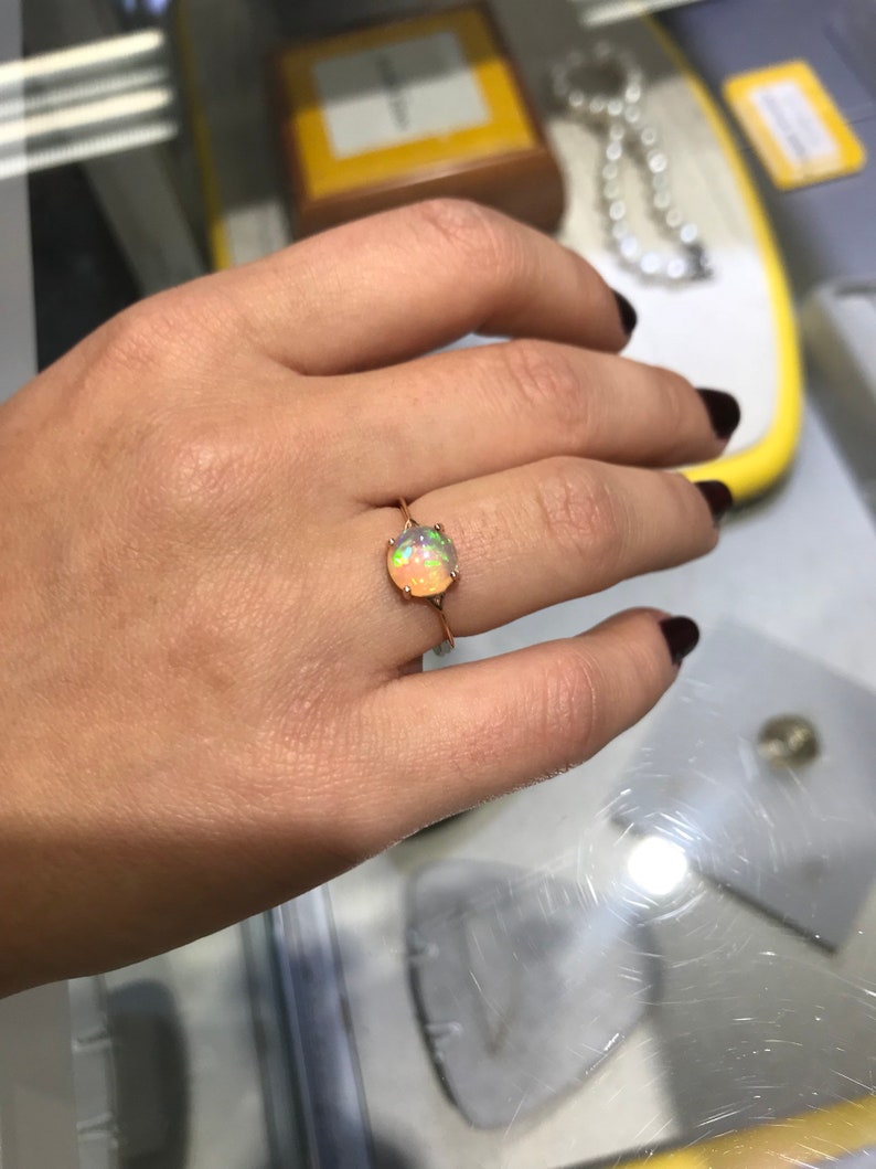 May include: A rose gold ring with a round, multi-colored opal gemstone.