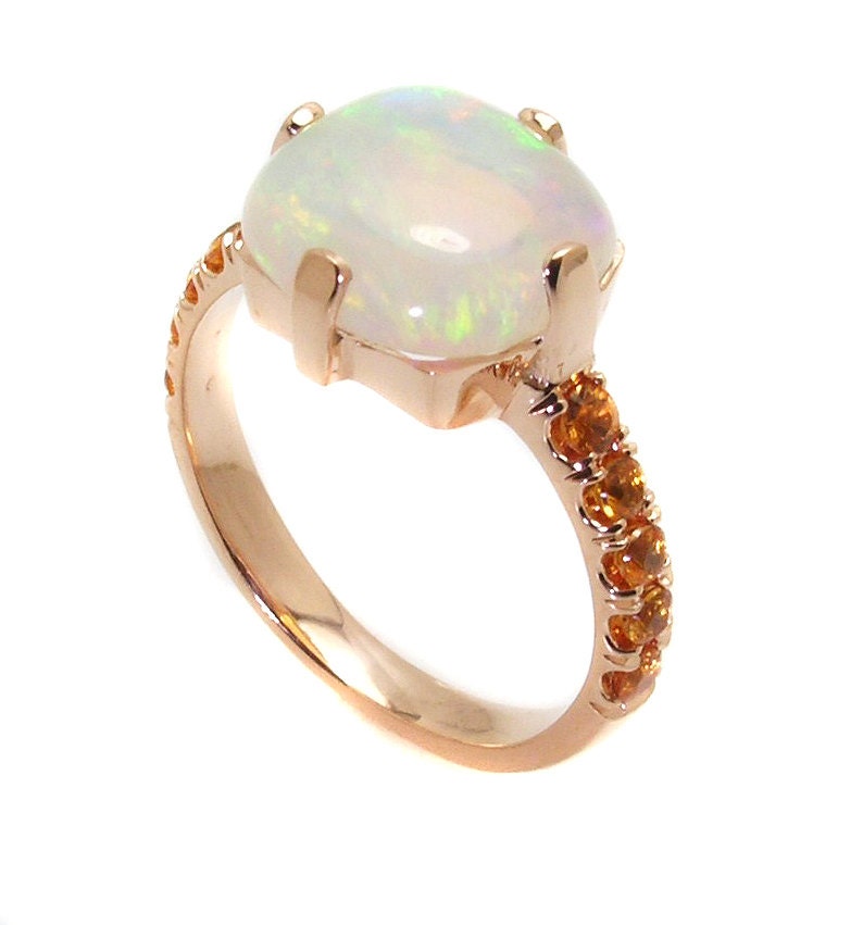 May include: A rose gold ring with a large white opal gemstone and a band accented with small orange gemstones.