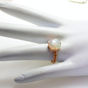 May include: A ring with a large white opal gemstone set in a rose gold band. The band is adorned with smaller gemstones.