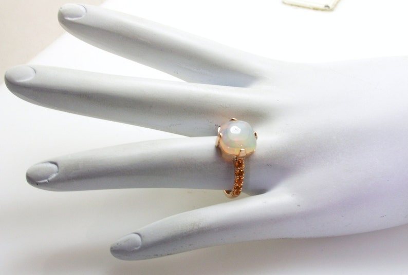 May include: A ring with a large white opal gemstone set in a rose gold band. The band is adorned with smaller gemstones.