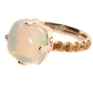 May include: A rose gold ring with a large white opal gemstone and a band accented with small orange gemstones.