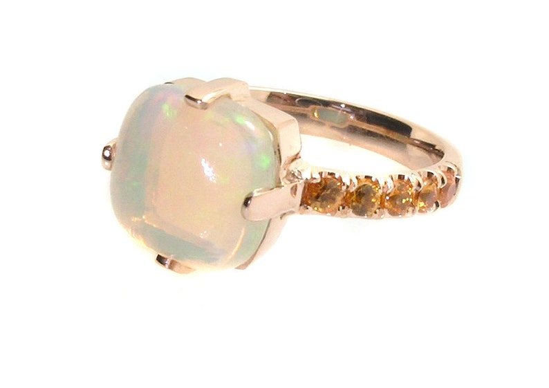 May include: A rose gold ring with a large white opal gemstone and a band accented with small orange gemstones.
