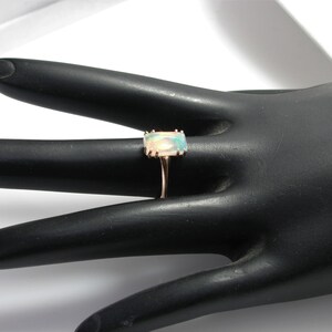 May include: A gold ring with a rectangular opal gemstone. The ring is set on a black ring display stand.