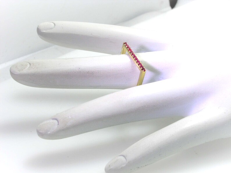 Op de afbeelding: Een gouden ring met een rechthoekige band bezet met kleine rode edelstenen.