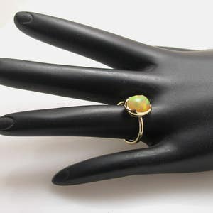 May include: A gold ring with a light green opal gemstone. The ring is on a black mannequin hand.