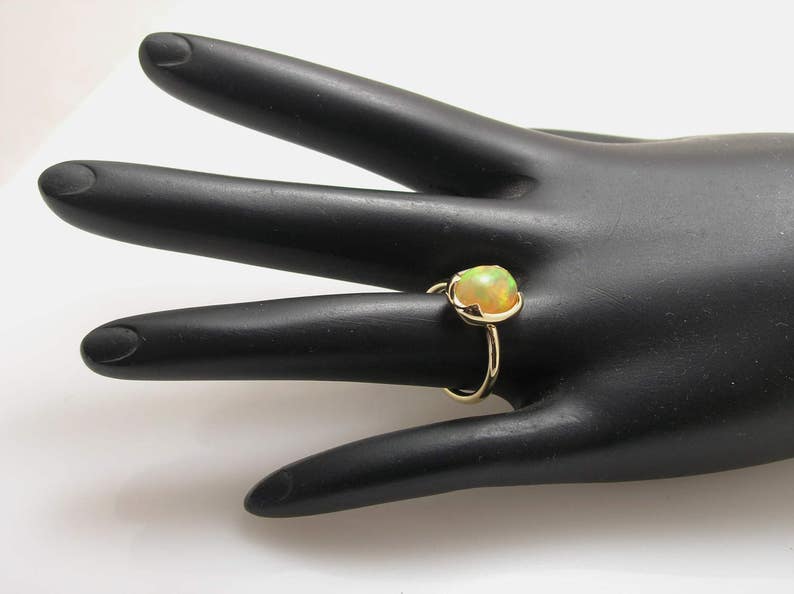 May include: A gold ring with a light green opal gemstone. The ring is on a black mannequin hand.
