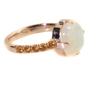 May include: A rose gold ring with a large white opal gemstone and a band of smaller orange gemstones.