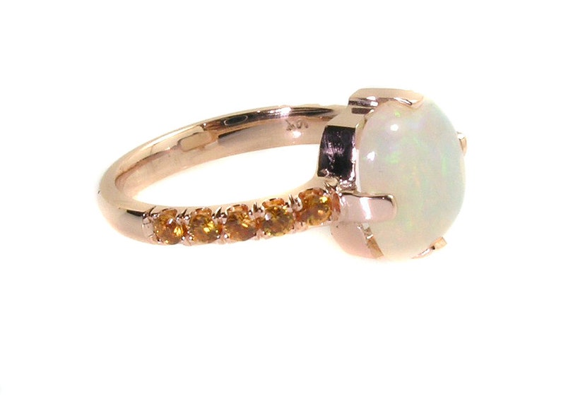 May include: A rose gold ring with a large white opal gemstone and a band of smaller orange gemstones.