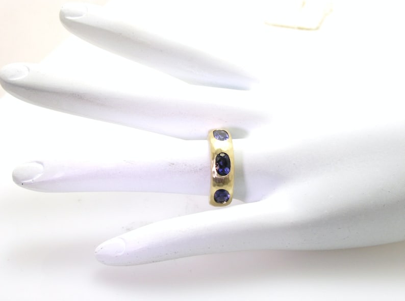 May include: A gold band ring with five blue oval-shaped gemstones set into the band.