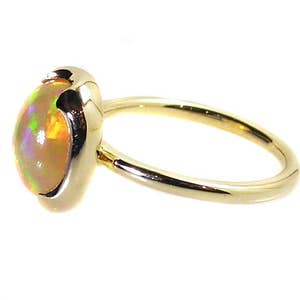 May include: A gold ring with a light yellow opal gemstone. The opal has a pearlescent sheen with hints of green and orange.