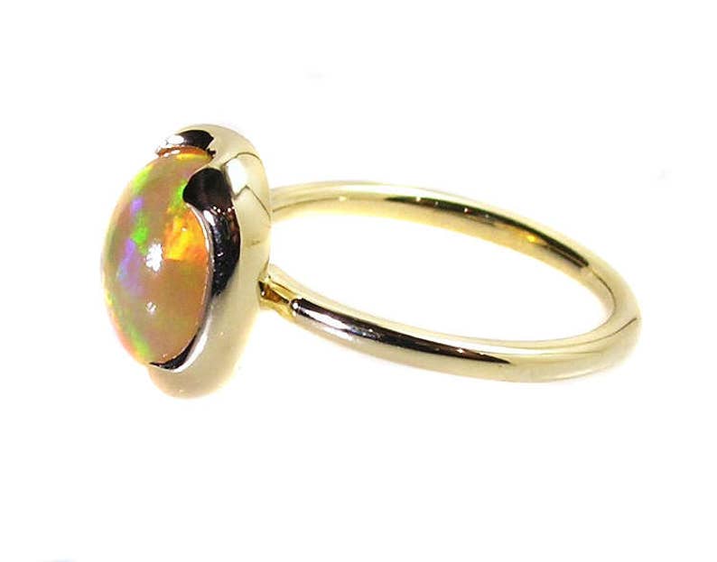 May include: A gold ring with a light yellow opal gemstone. The opal has a pearlescent sheen with hints of green and orange.