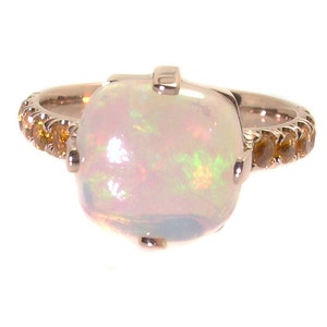 May include: A rose gold ring with a large white opal gemstone and a band of smaller yellow gemstones.