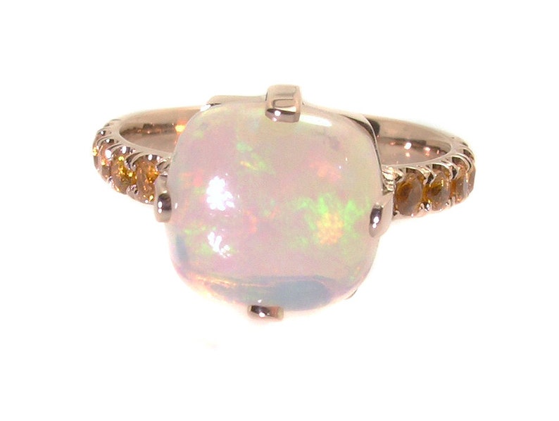 May include: A rose gold ring with a large white opal gemstone and a band of smaller yellow gemstones.