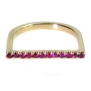 Op de afbeelding: Een gouden ring met een rechthoekige band bezet met een rij robijnen.