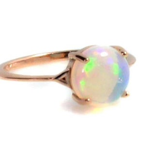 May include: A rose gold ring with a white opal gemstone. The opal has a rainbow iridescent sheen.