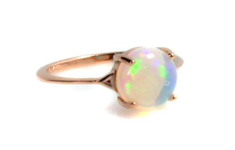 May include: A rose gold ring with a white opal gemstone. The opal has a rainbow iridescent sheen.
