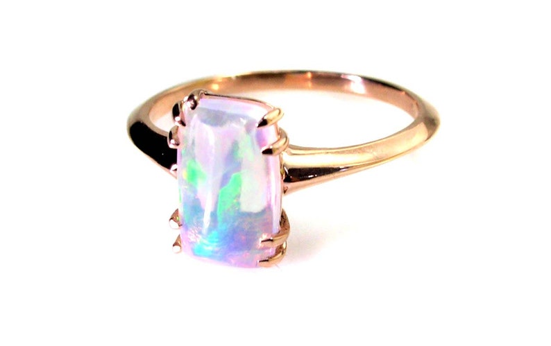 May include: A rose gold ring with a rectangular iridescent opal gemstone.