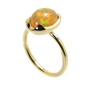 May include: A gold ring with a round, iridescent opal gemstone set in a delicate, curved setting.