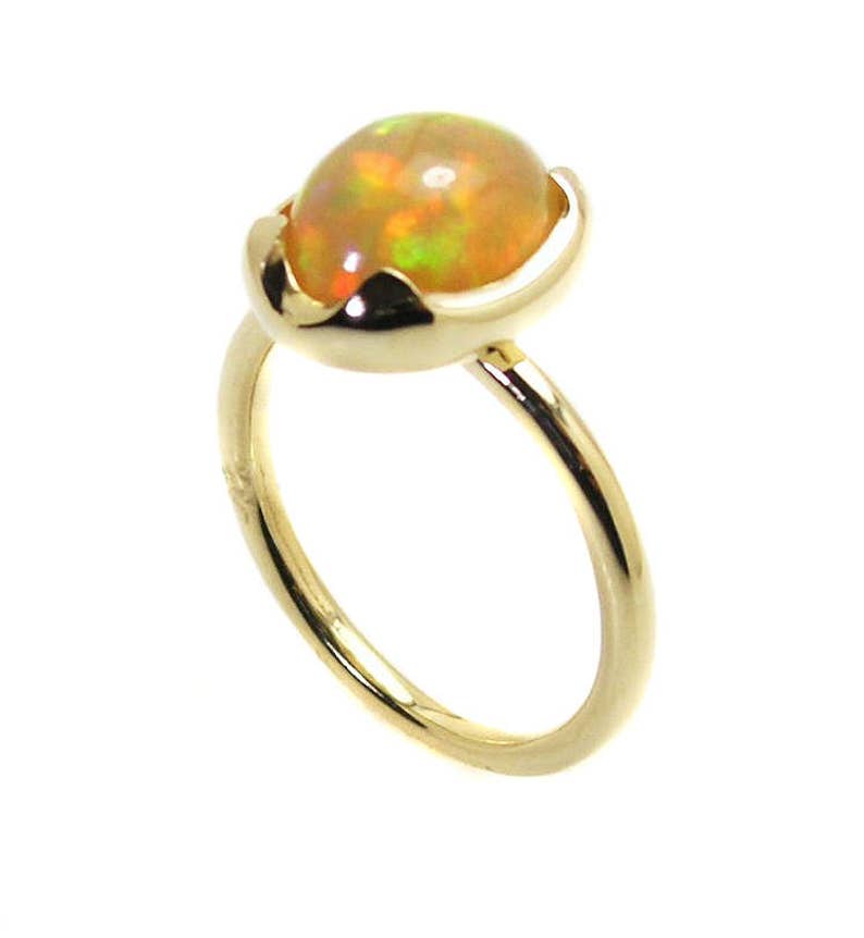 May include: A gold ring with a round, iridescent opal gemstone set in a delicate, curved setting.